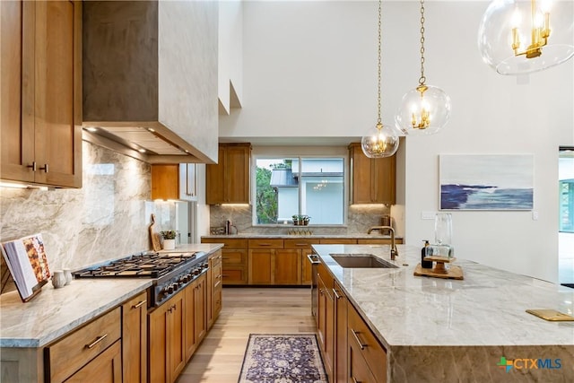 kitchen featuring brown cabinets, stainless steel gas stovetop, light wood-style flooring, a sink, and light stone countertops