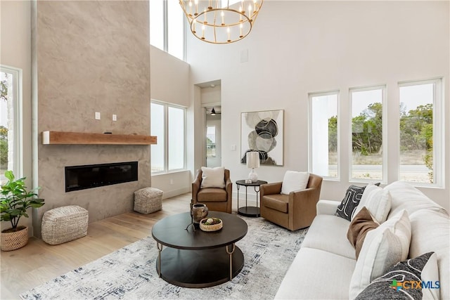 living area with a towering ceiling, an inviting chandelier, a fireplace, and wood finished floors