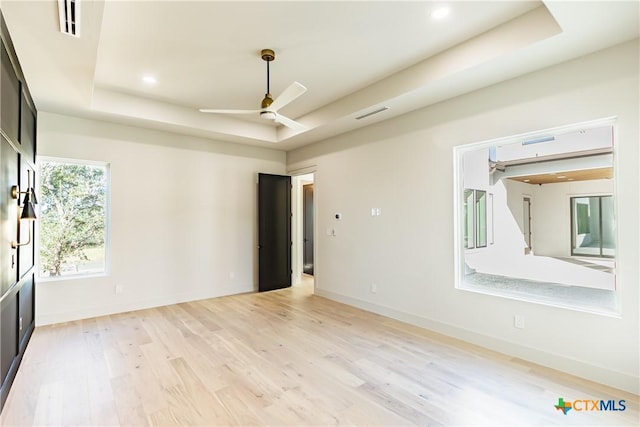 empty room featuring light wood-type flooring, ceiling fan, a tray ceiling, and baseboards