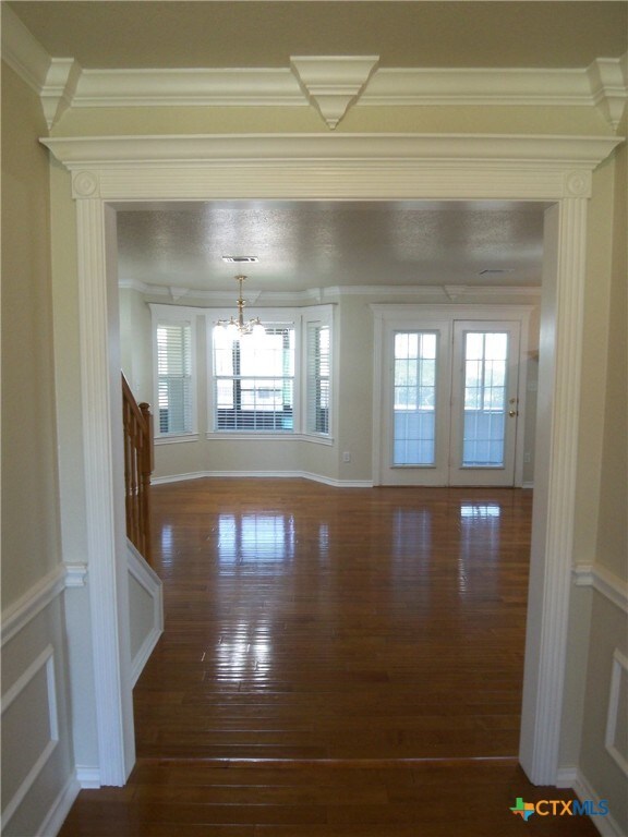 spare room featuring dark wood-type flooring, a chandelier, a healthy amount of sunlight, and crown molding