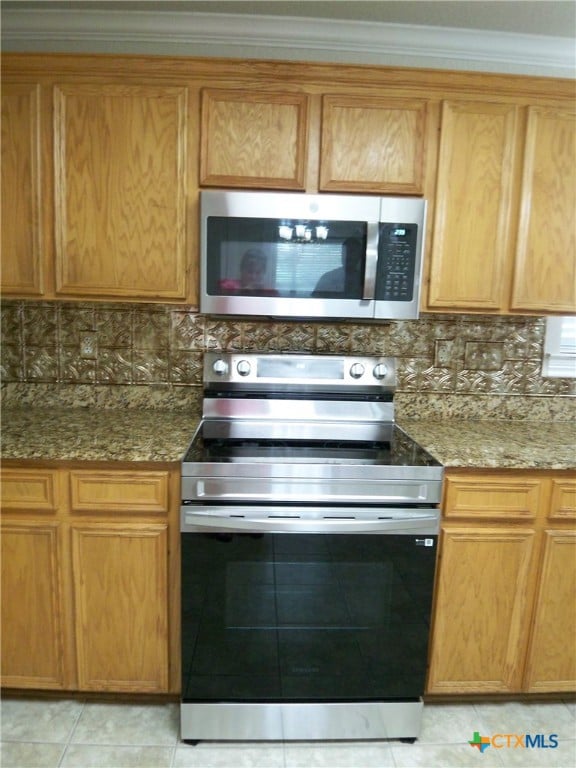 kitchen with appliances with stainless steel finishes, light tile patterned floors, backsplash, stone counters, and crown molding