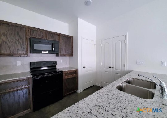 kitchen with dark brown cabinets, black appliances, sink, and light stone counters