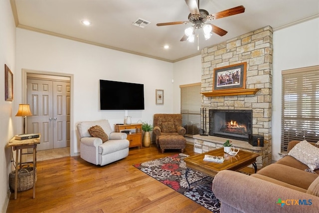 living room featuring hardwood / wood-style floors, ceiling fan, a stone fireplace, and crown molding