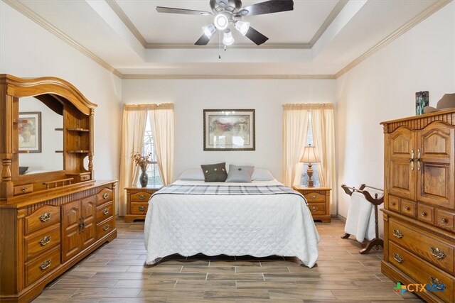 bedroom with ornamental molding, dark wood-type flooring, ceiling fan, and a tray ceiling