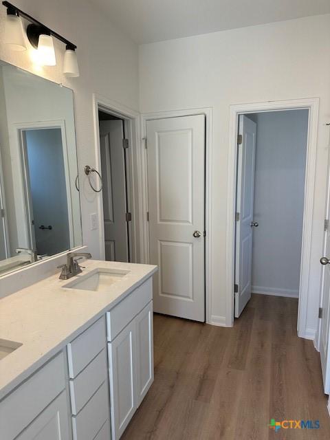 bathroom with double vanity, a sink, baseboards, and wood finished floors