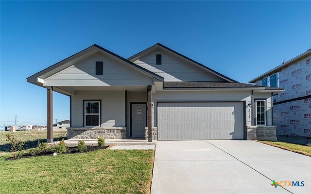 view of front of house with covered porch, a garage, and a front lawn