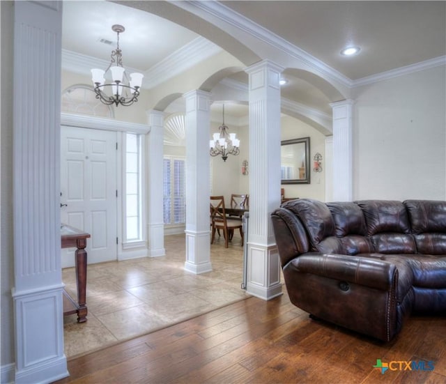 foyer entrance featuring ornate columns, ornamental molding, wood-type flooring, and an inviting chandelier