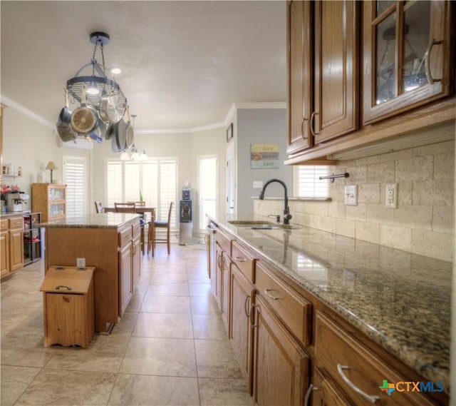 kitchen with tasteful backsplash, brown cabinets, light stone countertops, crown molding, and a sink