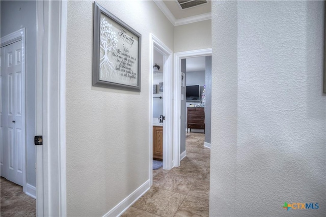 hall with a textured wall, visible vents, baseboards, ornamental molding, and tile patterned floors