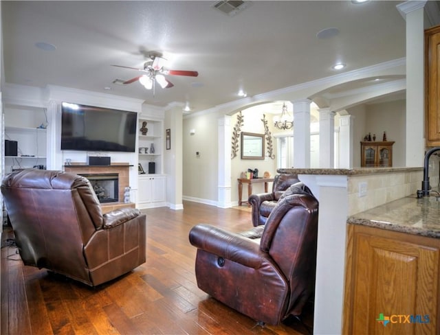 living room featuring arched walkways, dark wood finished floors, decorative columns, visible vents, and a tiled fireplace