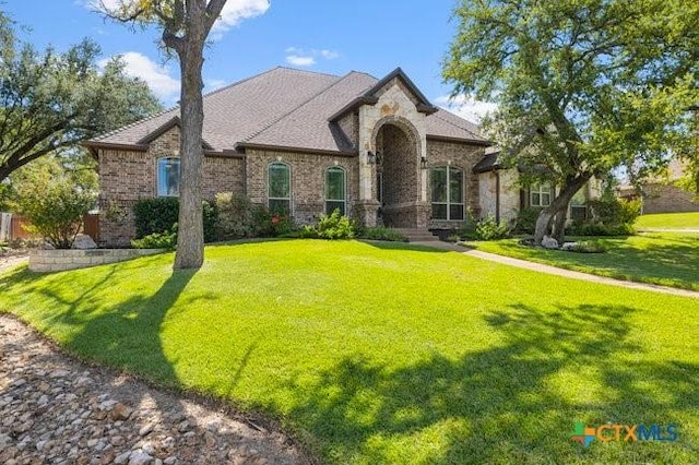 french provincial home with brick siding and a front yard