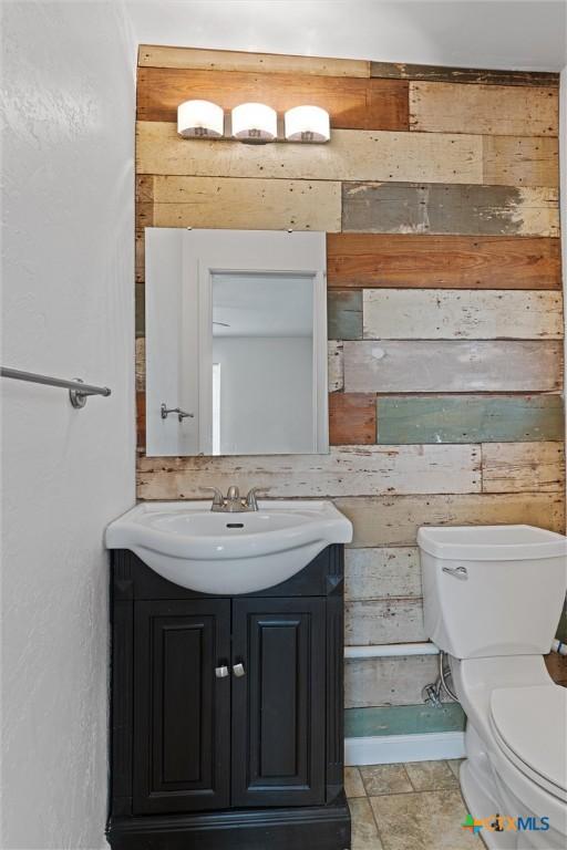 bathroom with toilet, vanity, and wood walls