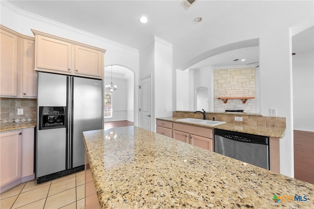 kitchen with sink, light stone counters, appliances with stainless steel finishes, crown molding, and decorative backsplash