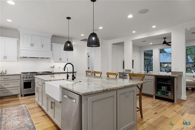 kitchen featuring a center island with sink, wine cooler, appliances with stainless steel finishes, a kitchen bar, and light hardwood / wood-style floors