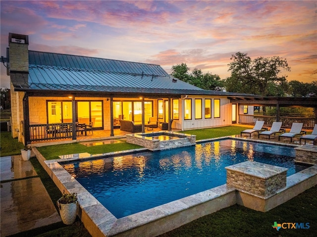 pool at dusk with a patio area, a yard, and an in ground hot tub