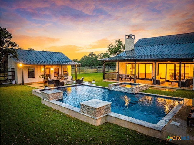 pool at dusk featuring a lawn, a patio, and an in ground hot tub