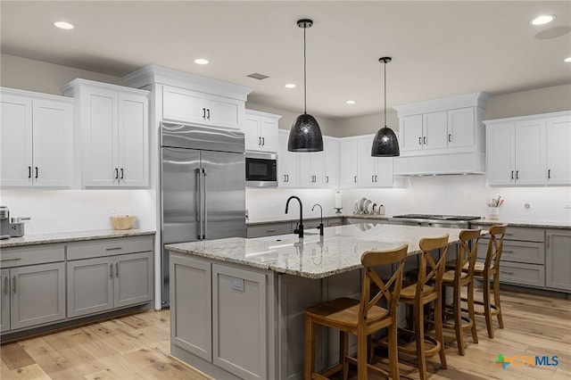 kitchen with pendant lighting, light hardwood / wood-style floors, built in appliances, and a kitchen island with sink