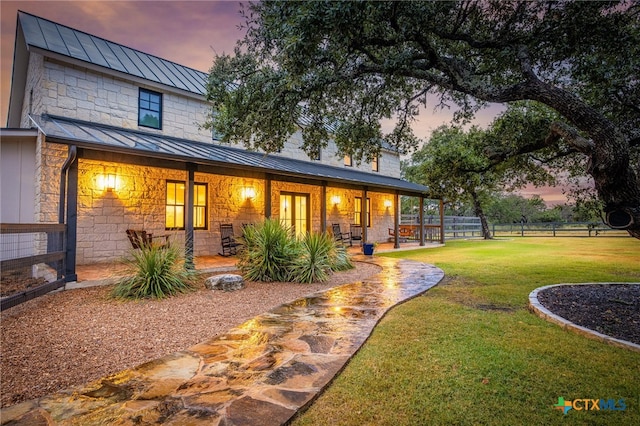 back house at dusk with a lawn and a patio area