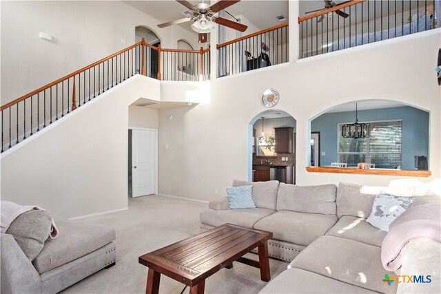 carpeted living room with a towering ceiling and ceiling fan with notable chandelier