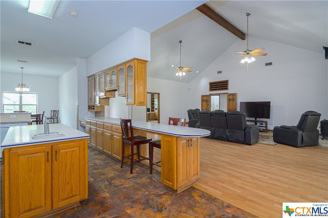 kitchen featuring beamed ceiling, a breakfast bar area, ceiling fan with notable chandelier, a center island, and dark wood-type flooring