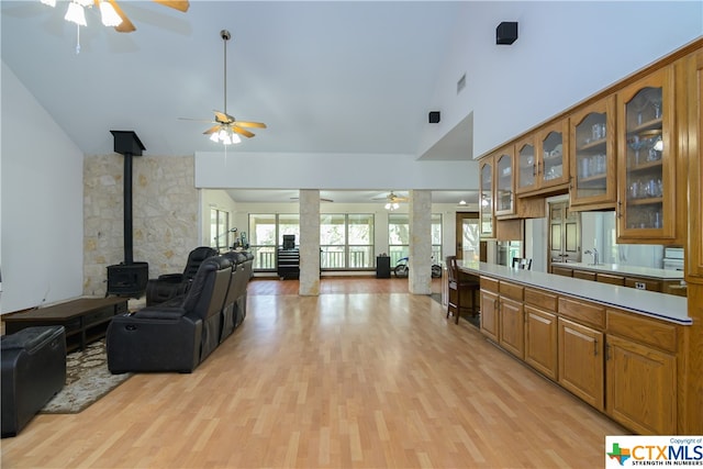 interior space featuring high vaulted ceiling, ceiling fan, a wood stove, and light hardwood / wood-style floors