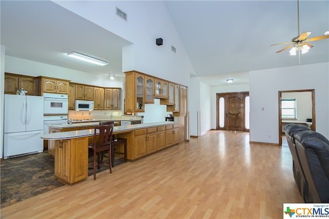 kitchen with high vaulted ceiling, ceiling fan, a breakfast bar, light hardwood / wood-style flooring, and white appliances