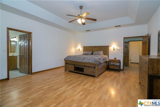 bedroom with light hardwood / wood-style flooring, ceiling fan, a tray ceiling, and connected bathroom