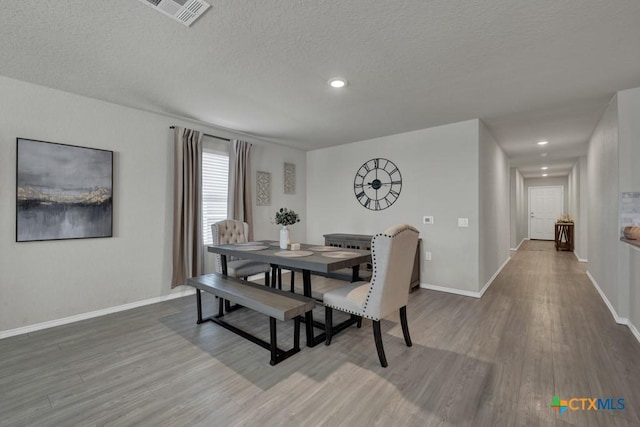 dining space featuring a textured ceiling, wood finished floors, baseboards, and visible vents