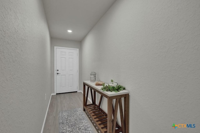corridor with wood finished floors, a textured wall, baseboards, and recessed lighting