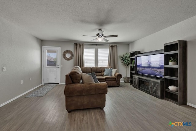 living area featuring a textured ceiling, wood finished floors, ceiling fan, and baseboards
