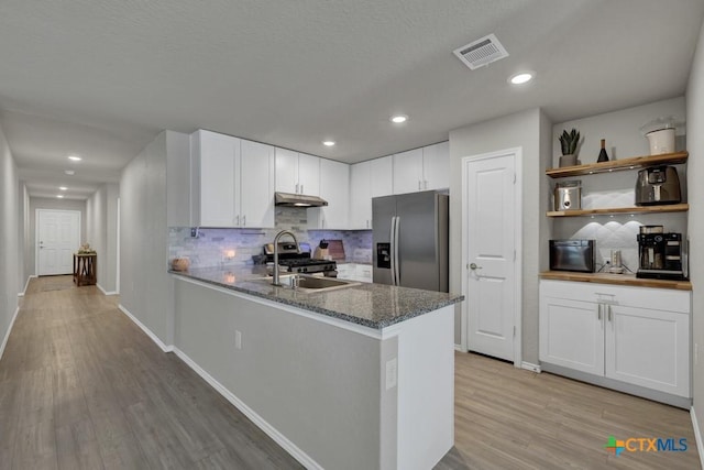 kitchen with white cabinets, stainless steel refrigerator with ice dispenser, a sink, under cabinet range hood, and gas stove