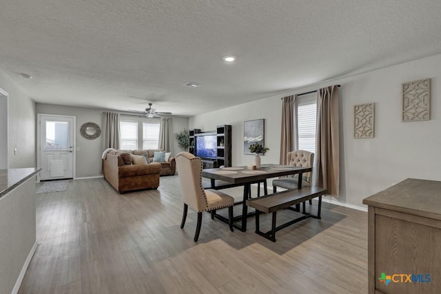 dining room featuring light wood-type flooring, baseboards, a textured ceiling, visible vents, and ceiling fan
