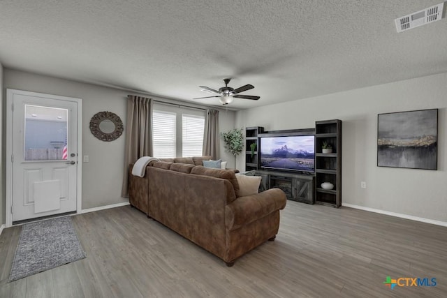 living room with visible vents, ceiling fan, light wood finished floors, and a textured ceiling