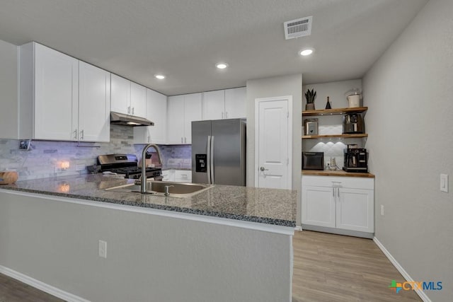 kitchen with dark stone countertops, a peninsula, decorative backsplash, stainless steel appliances, and a sink