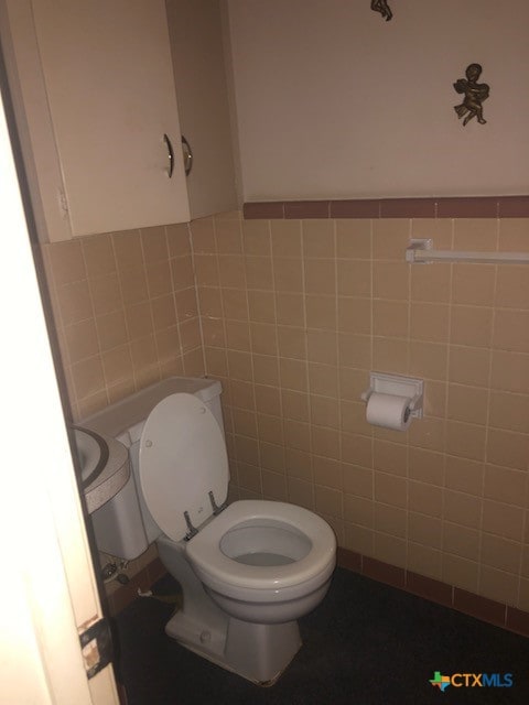 bathroom with toilet and tile walls