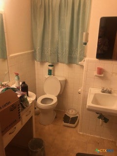 bathroom featuring tile patterned flooring, sink, tile walls, and toilet