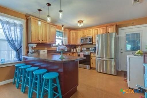 162 Canyon Crk, Canyon Lake, TX 78133 - kitchen featuring visible vents, a peninsula, appliances with stainless steel finishes, light brown cabinets, and a breakfast bar area