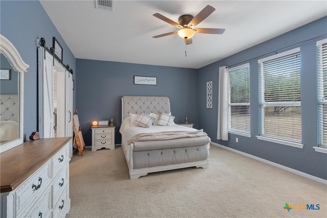 carpeted bedroom featuring a barn door and ceiling fan