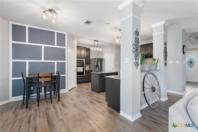 kitchen with stainless steel appliances, a kitchen island, light wood-type flooring, decorative light fixtures, and dark brown cabinetry