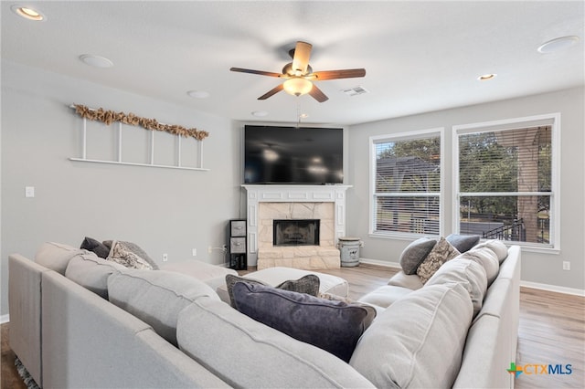 living room with ceiling fan, a stone fireplace, and light hardwood / wood-style flooring