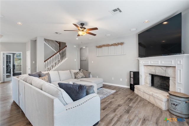 living room featuring a stone fireplace, light wood-type flooring, and ceiling fan