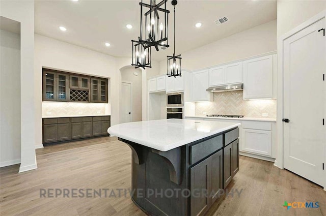 kitchen featuring visible vents, white cabinetry, decorative backsplash, and under cabinet range hood