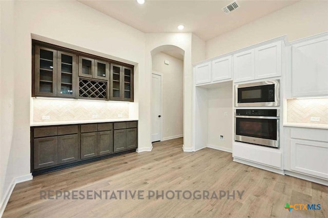 kitchen with built in microwave, decorative backsplash, oven, visible vents, and arched walkways