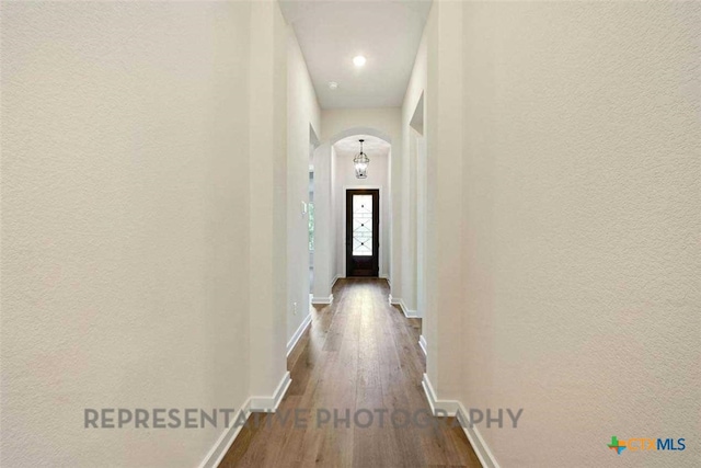 hall featuring arched walkways, a textured wall, baseboards, and dark wood-type flooring