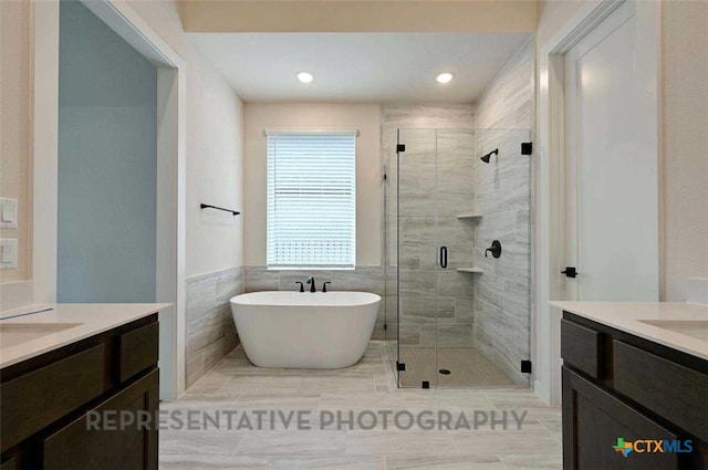 full bathroom featuring a soaking tub, a stall shower, two vanities, recessed lighting, and tile walls