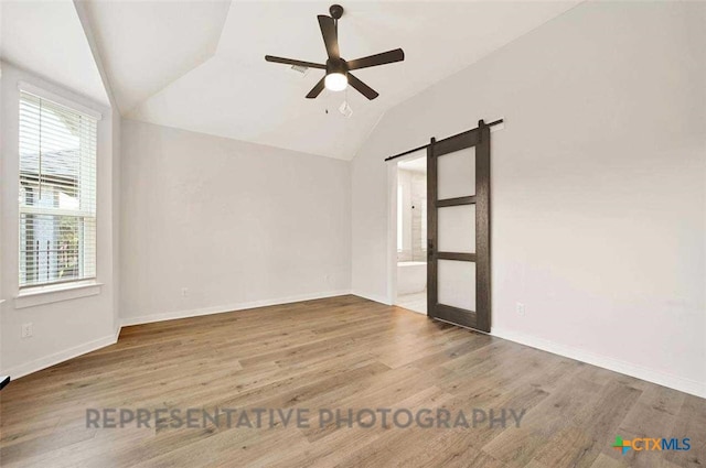 empty room with a ceiling fan, vaulted ceiling, a barn door, and a healthy amount of sunlight