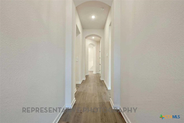 corridor featuring dark wood-style floors, recessed lighting, a textured wall, baseboards, and arched walkways
