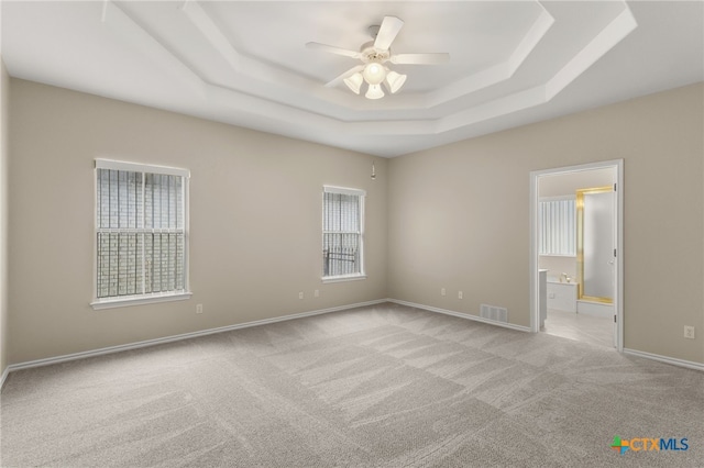 unfurnished bedroom featuring visible vents, a raised ceiling, baseboards, connected bathroom, and light carpet
