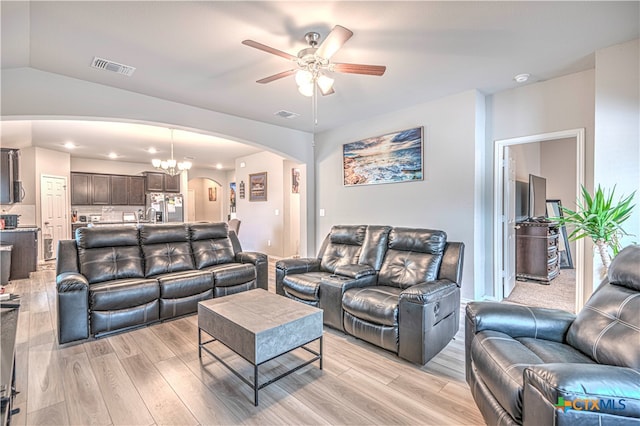 living room with ceiling fan with notable chandelier, vaulted ceiling, and light wood-type flooring