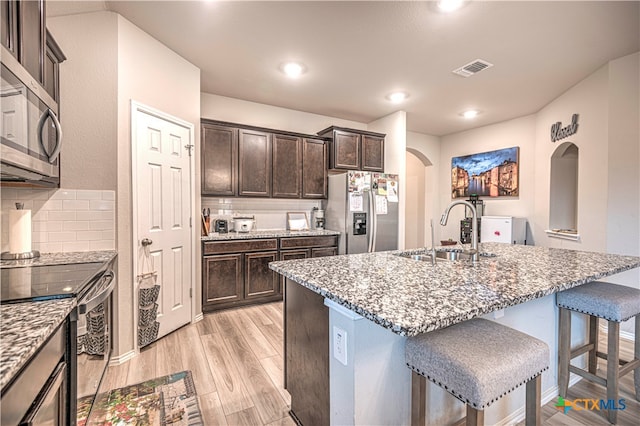 kitchen with appliances with stainless steel finishes, sink, light hardwood / wood-style floors, and an island with sink